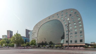 Rotterdamse Markthal 'ın dış yüzeyinde aşırı kayma. Dükkanları ve restoranları olan ikonik at nalı şeklinde bir bina. Meydanda gezinen insanlar. Gökdelenler ve arka planda canlı bir şehir manzarası