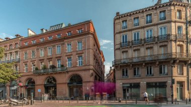 Toulouse, Occitanie, Fransa 'da Rue de Metz' in zaman çizelgesini gösteren panorama, tarihi cepheleri, dükkanları, kafeleri, trafiği ve mavi bulutlu gökyüzünü gösteriyor. Şehrin göbeğinde canlı bir şehir manzarası