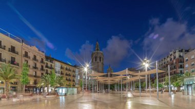 İspanya, Valencia 'daki Plaza de la Reina' da panoramik günden geceye geçiş süreleri aşırı hızlanıyor. Tarihi bir kilise kulesi, hareketli kafeleri ve akşam gökyüzünün altında merkezi bir çeşmesi olan canlı bir meydan..