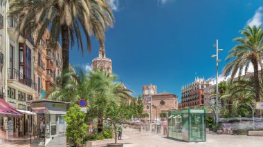 Valencia, İspanya 'da Plaza de la Reina' nın panoramik zaman atlaması. Tarihi bir kilise kulesi, hareketli kafeler ve sıcak Akdeniz semaları altında palmiyeleri olan merkezi bir çeşme..