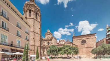 Valencia, İspanya 'da Plaza de la Reina' nın panoramik zaman atlaması. Tarihi bir kilise kulesi, hareketli kafeler ve sıcak Akdeniz mavi bulutlu gökyüzünün altında merkezi bir çeşme ile dolu canlı bir meydan..