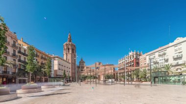 Panorama, İspanya, Valencia 'daki Plaza de la Reina' nın zaman çizelgesini gösteriyor. Tarihi bir kilise kulesi, hareketli kafeler ve sıcak Akdeniz mavi gökyüzünün altında merkezi bir çeşmesi olan canlı bir meydan..