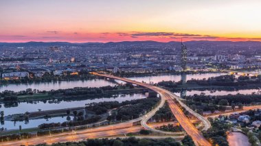Viyana üzerinde gökdelenler, karayolu kavşağı ve Avusturya 'daki nehir kenarından geceye geçiş yapan hava panoramik manzarası. Akşam üstü Tuna Kulesi 'nden gün batımından sonra gökyüzü