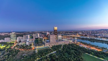 Donau City gökdelenleri, tarihi binalar ve Avusturya 'da gece gündüz nehir kenarındaki gezinti güvertesi ile Viyana üzerinde havadan panoramik bir manzara. Akşam üstü Tuna Kulesi 'nden gün batımından sonra gökyüzü