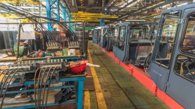 Konveyör montajı, traktörün gövdesini büyük endüstriyel fabrika zaman diliminde sahneleyecek. Kabin montajı, kurulum parçaları özel bir masada.