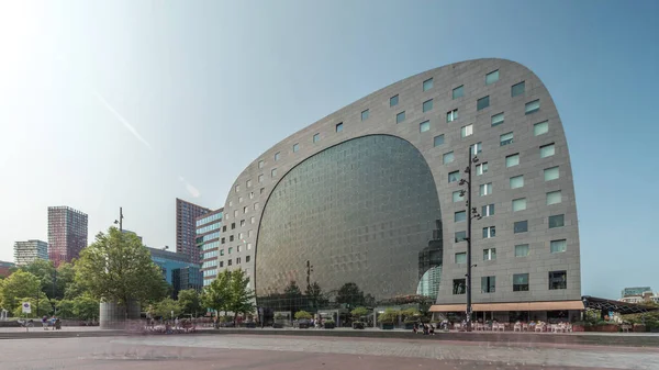 Rotterdamse Markthal 'ın dış yüzeyinde aşırı kayma. Dükkanları ve restoranları olan ikonik at nalı şeklinde bir bina. Meydanda gezinen insanlar. Gökdelenler ve arka planda canlı bir şehir manzarası