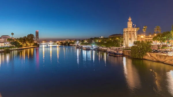 İspanya, Seville 'deki Torre del Oro gözlem kulesi yakınlarındaki Guadalquivir Nehri boyunca yüzen bir tur teknesi. Günbegün geçiş zamanı, şehrin ışıkları su ve deniz manzarasını yansıtıyor.