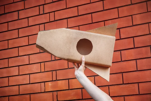 Cardboard space rocket in hand against brick wall — Stock Photo, Image