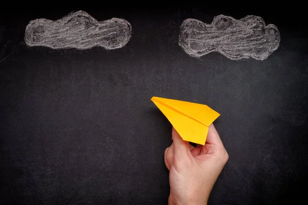 Hands holding yellow paper plane under clouds — Stock Photo, Image