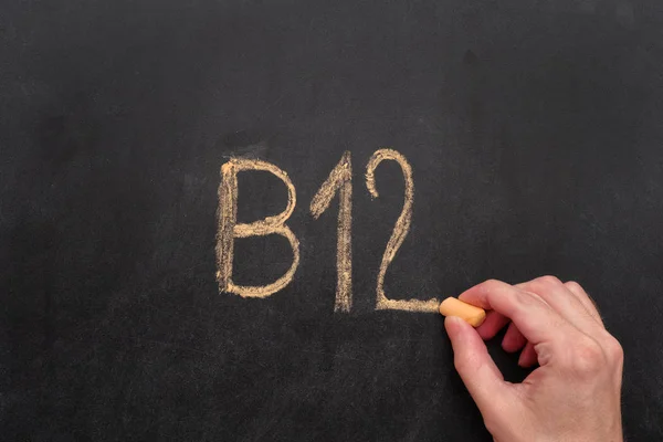Чоловік пише слово B12 на дошці — стокове фото