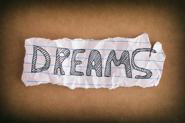 Crumpled piece of paper with the word Dreams on brown paper back — Stock Photo, Image