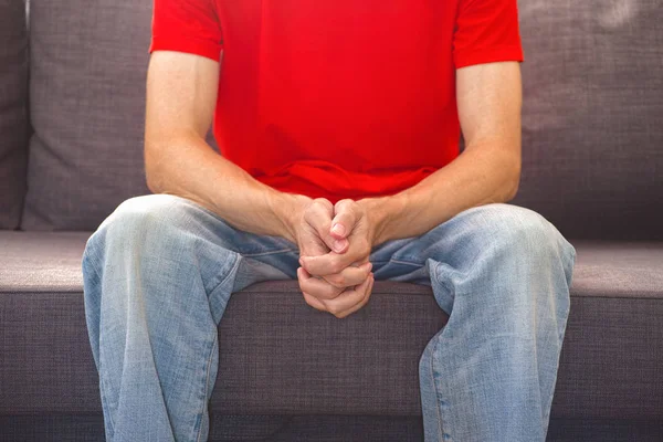 Young man sitting on couch and holding his hands together — Stock Photo, Image