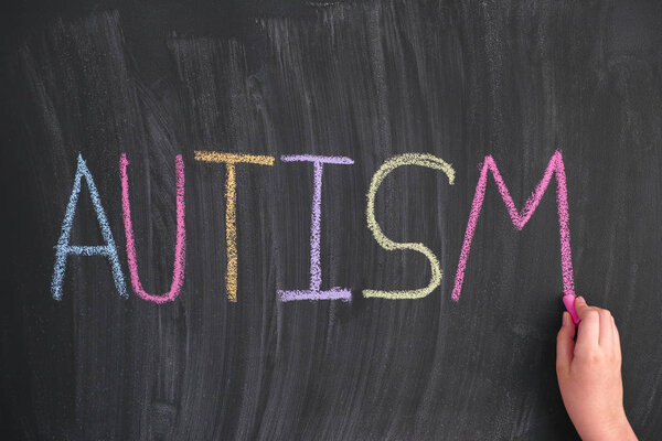 Child writing the word Autism on a blackboard