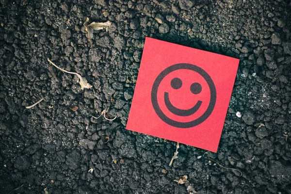 Nota de papel vermelho com rosto feliz no fundo do solo — Fotografia de Stock