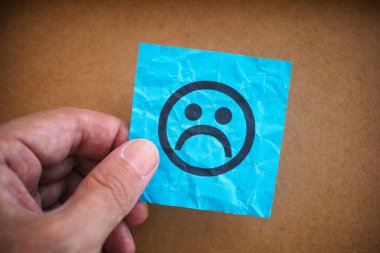 Elinde mavi kâğıt bir notla elinde üzgün bir yüz olan bir adam. Kapat..