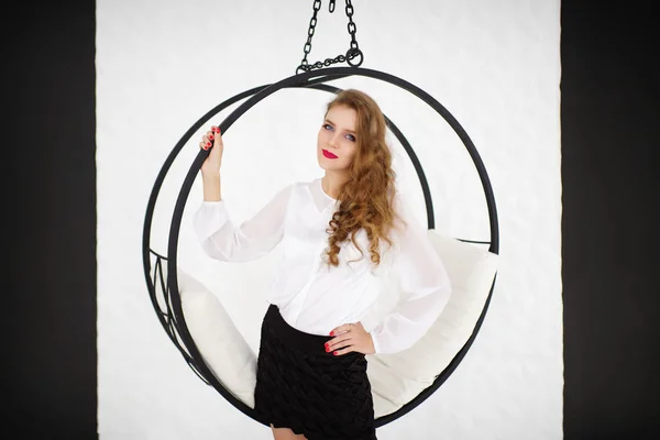 Beautiful girl holds on to the round swing. Creative design, conceptual idea concept, horizontal banner. White silk blouse with flared sleeves, black mini skirt. Red nails manicure, new bright make-up