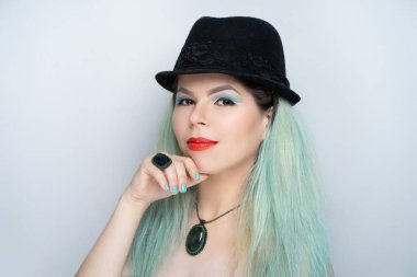 Güzel kız mavi saçlı aqua, manikür tasarımı nane renk oje, resmi olmayan bir görünüme sahip. Klasik siyah şapka Melon derby bir beyefendi gibi. Çenesi dokunmatik. Düşünceli gizemli sırıtış