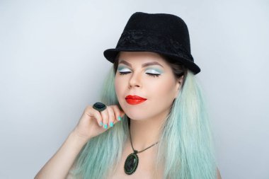 Güzel kız mavi saçlı aqua, manikür tasarımı nane renk oje, resmi olmayan bir görünüme sahip. Klasik siyah şapka Melon derby bir beyefendi gibi. Çenesi dokunmatik. Düşünceli gizemli sırıtış