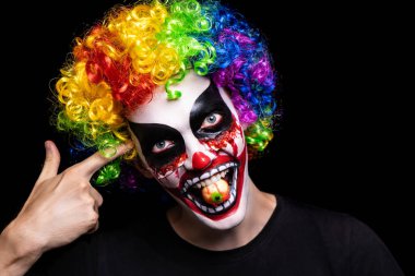Cadılar Bayramı için korkutucu palyaço makyaj. Cilt yarasından akan kan yanaklarda, kes. Lolipop göz şeklinde. Korkunç kabuslar dehşeti. Büyük kıvırcık peruk gökkuşağı. Kanlı ağız diş boyalı