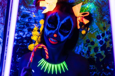 Cadılar Bayramı için korkutucu palyaço makyaj. Yanakları kırmızı burun, yarasından akan kan ağız deriyi kesme. Lolipop yalamak. Dehşet korkunç kabuslar. Büyük portakal iki ponytails bağlı saç yay. Komik surat