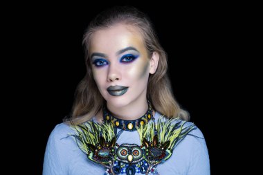 Yeşil orman kadın sanat makyaj. Komik resim bir Cadılar Bayramı partisi afiş için. Yaratıcı makyaj, büyük boncuk demir kolye. Gerdanlık baykuş gözleri iri ve kabarık tüyleri ile. Mavi parlak parlak gölgeler