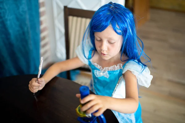 The little mermaid girl is interested in science. She sits at a large wooden table, looks through a microscope, studying biology and microbes. Blue dress and big wig artificial hair, halloween party
