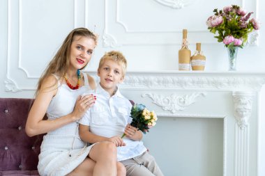 Kadın oğluyla birlikte kanepede oturuyor. Mutlu aile portresi, bakım, karşılıklı kavramını destekler. Onun sevgili kadın tarihinde 8 Mart, anneler günü parti, Happy Birthday tebrik ediyorum. Beyaz Oda