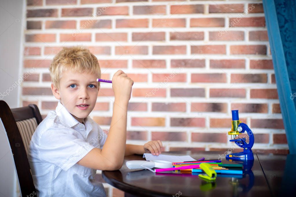 Happy cheerful boy came up with an idea. Young pupil student is sitting in a room near a brick wall, on the table are scattered markers and office supplies. Educational system lifestyle of new people