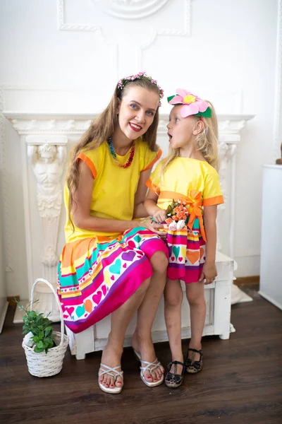 Style summer family look. Mom and daughter love. Take care of the child and ensure a happy childhood. Fun holidays. Bright yellow pink dress and floral decorations. White professional studio banner