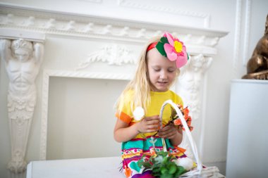 Güzel kız giyiyor parlak sarı elbise, pembe süs, aksesuar. Anneler günü tebrik ederim. Eğlenceli ve neşeli bir çocuk. Beyaz sepet çiçekli. Gülümse ve iyi bir ruh hali için pozitif sürpriz