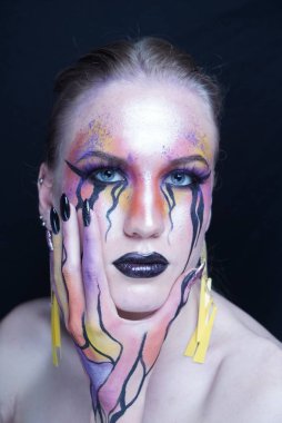 Mükemmel yüz genç güzel kız yüzüne dokunmadan, parlak makyaj, yüz yüze akan boyalar mor turuncu sarı çizgiler, maskara gözyaşları gözlerden akar. Uzun küpe, manikür siyah çivi