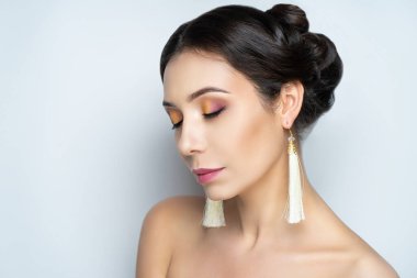 Saçı gür güzel bir kızın yakın plan portresi. Lüks saç modelleme. Orta boylu, siyah saçlı bir kadın. Düğün saç stili kıvırcık saç topladı. Güzel gelin tarzı yaratıcı takı küpeleri.