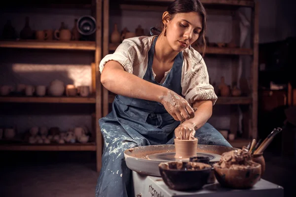 Hermoso escultor ceramista trabaja con arcilla en una rueda Potters y en la mesa con las herramientas. Producción artesanal . — Foto de Stock
