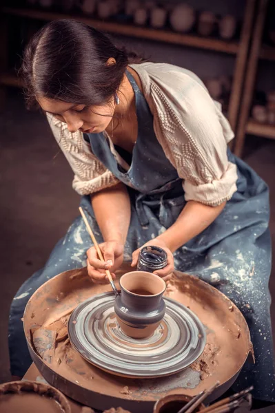 Mulher de cerâmica elegante situada no banco com roda de cerâmica e fazendo panela de barro. Artesanato nacional . — Fotografia de Stock