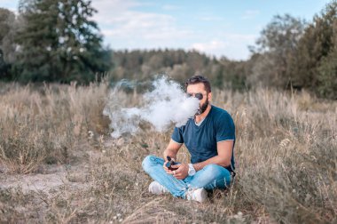 Acımasız adam elektronik sigara içiyor ve duman bulutu soluyor. Vaping kavramı.