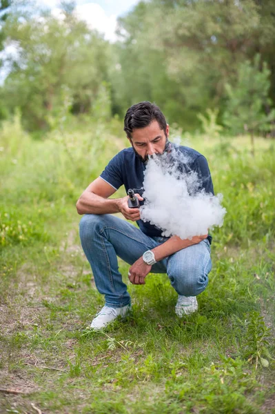 Şık vahşi adam ormanda elektronik bir sigara vaping. Sigara içilmeyen. — Stok fotoğraf