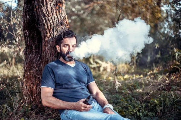 Bel vagabondo che si gode una sigaretta elettronica. All'uomo piace molto il processo di fumo. . — Foto Stock