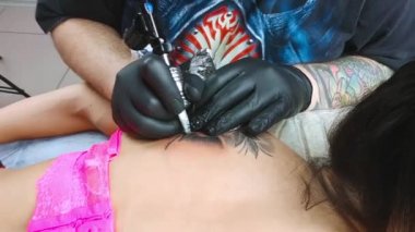 Siyah eldivenli bir dövme sanatçısı bir kadının omzuna dövme yaptırdı.