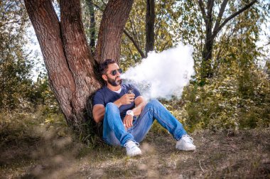 Kendine güvenen vaper orman zemininde bir çift bir vape havaya uçurrıyor. Elektronik sigara konsepti.