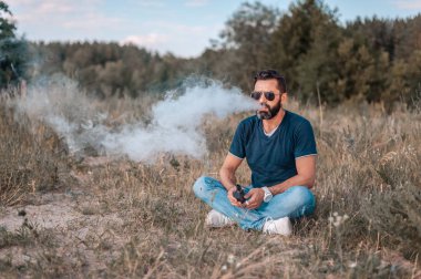 Temiz havada şık sakallı vaper bir elektronik duman cihazı sigara. Vaping.
