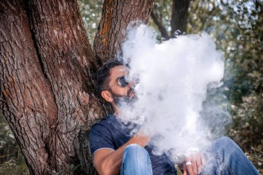 Modern vape adam ormanda elektronik bir duman cihazı sigara. Adam gerçekten sigara sürecini seviyor.