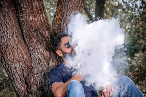 Moderno vaporizzatore che fuma un dispositivo elettronico di fumo nel bosco. All'uomo piace molto il processo di fumo. . — Foto Stock