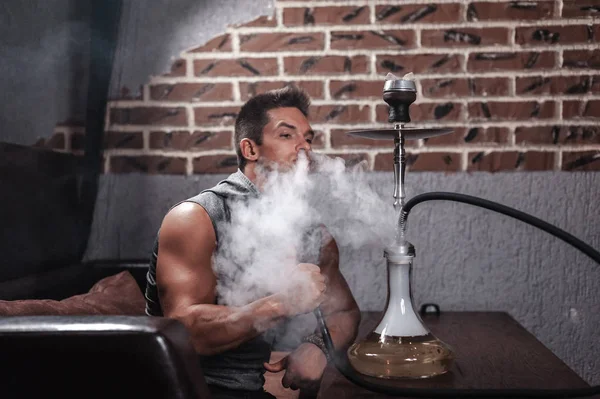 Brutale ragazzo sta soffiando fumo nel tubo shisha . — Foto Stock