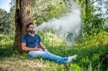 Şık vape adam ormanda bir çift elektronik sigara havaya uçurrıyor. Yakışıklı adam.