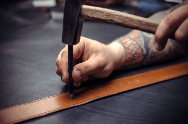 Handicraftsman processing a leather workpiece at the workshelf clipart