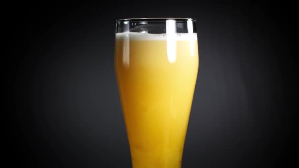 Piwo wlewa się do szklanki na czarnym tle. Bursztynowe piwo jest uwodzicielsko wlewane do szklanki piwa — Wideo stockowe
