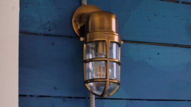 Ahşap bir binanın gri duvarında siyah metal ızgara olan cam bir sokak lambası. Sokak ışıkları.