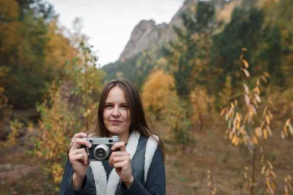 Portrait of a girl with a retro camera on the background of autumn mountains