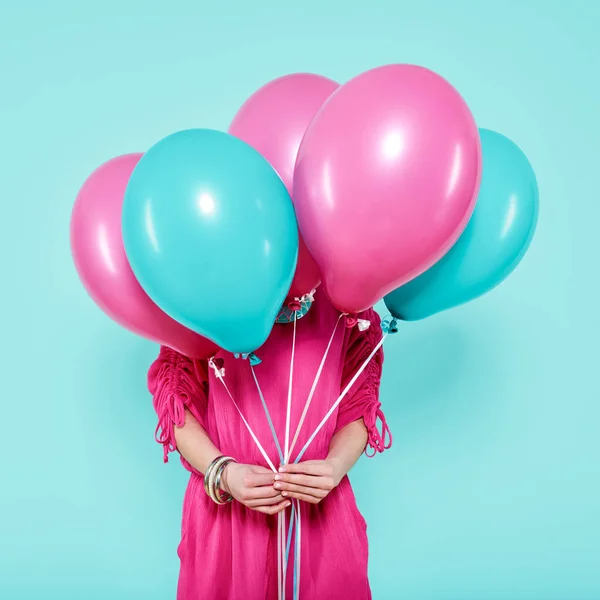 Gorgeous young woman in party outfit holding bunch of colourful balloons, isolated over pastel blue colored background. Birthday Party concept.