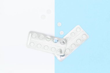 White pills and blister pack on blue pastel colored background. Pharmaceutical industry minimal still life flat lay background. Opioid epidemic and drug abuse concept. clipart